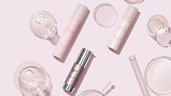 Three Mary Kay serums lying on a pink surface with scientific glassware