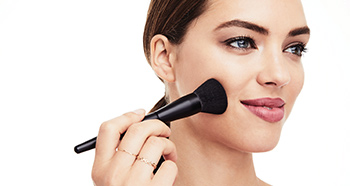 A brunette woman applies Mineral Powder Foundation using the Powder Brush.